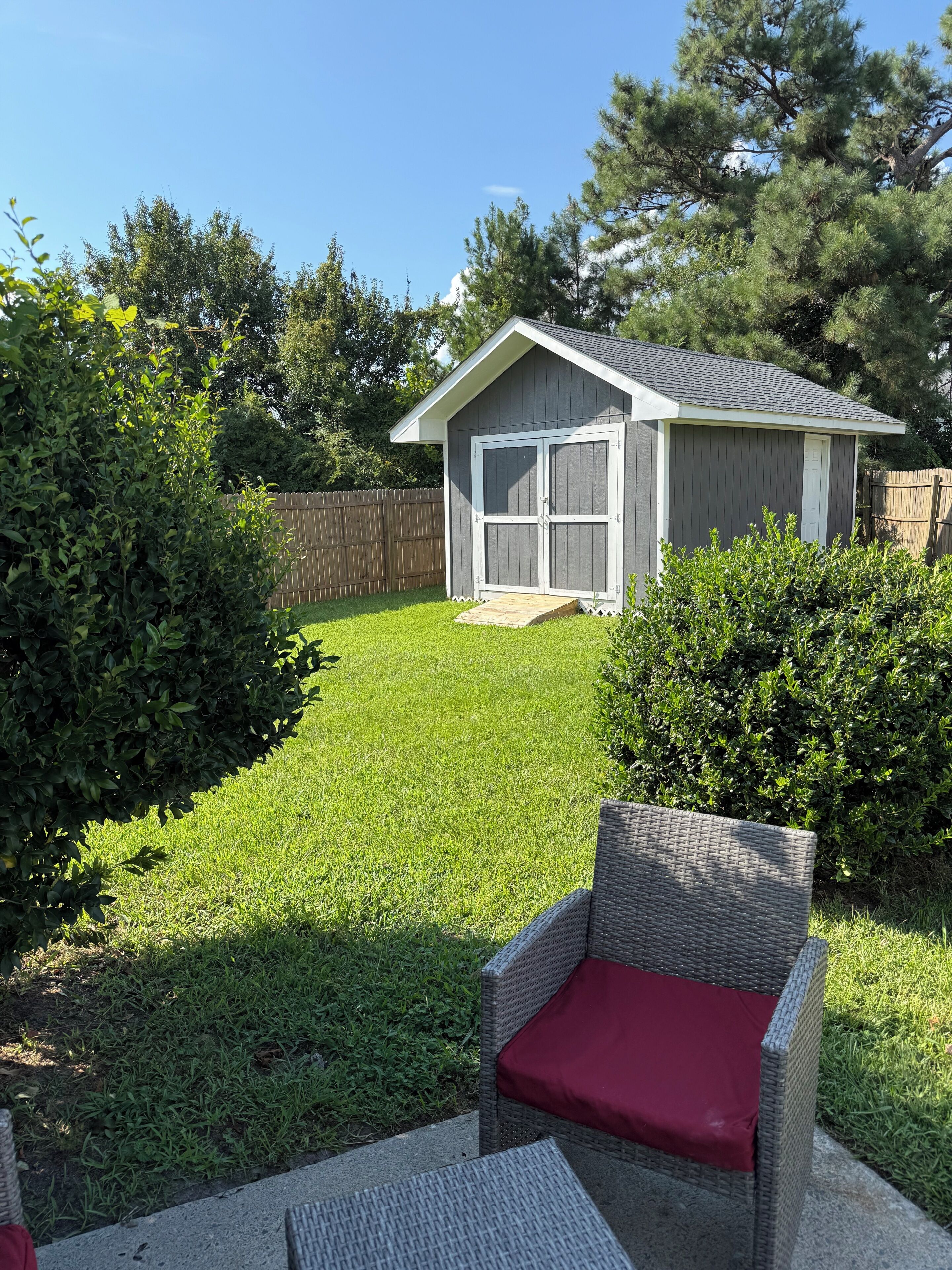 Ein Garten mit Gartenhaus, Terrassenstuhl und gepflegtem Rasen.