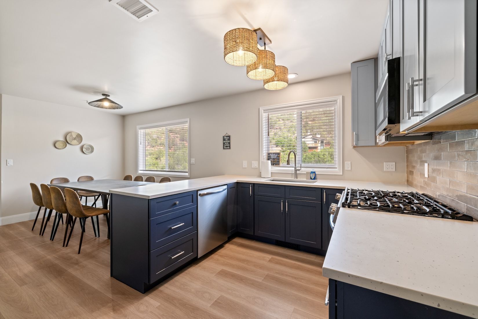 Une cuisine moderne dotée d’un îlot central, de meubles de couleur sombre, d’une cuisinière à gaz et de luminaires suspendus.