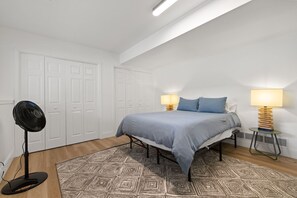 A bedroom with a bed, two bedside lamps, a standing fan, and a patterned rug.