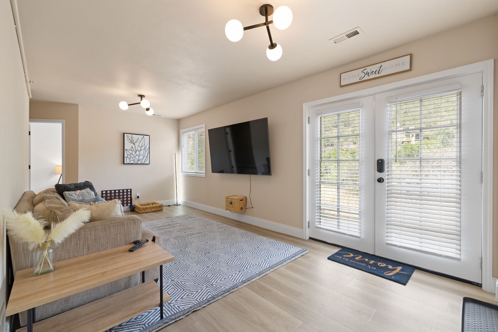 A living room with a sofa, a coffee table, a flat-screen TV, a fireplace, and a large window with blinds.