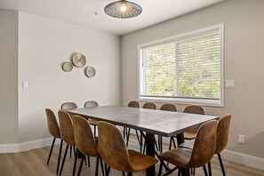 A dining area with a rectangular table surrounded by six chairs, a large window with blinds, and three wall-mounted decorative plates.