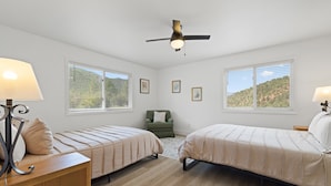 Una camera da letto con due letti, un ventilatore a soffitto e ampie finestre che offrono vista su un paesaggio collinare.