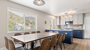 Una cucina moderna con isola centrale, zona pranzo con tavolo e sedie in legno e ampie finestre dotate di persiane.