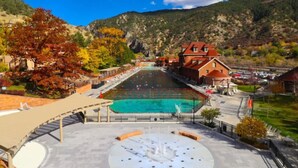 Una piscina con bordo circostante e fontana, con montagne e foglie autunnali sullo sfondo.