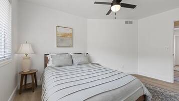 Une chambre à coucher avec un lit, un ventilateur de plafond, une lampe et un tableau accroché au mur.