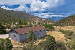 A two-story house with a red roof, surrounded by a dry grassy field and trees, with mountains in the background. - Renovated 6BR GWS Escape Near Aspen - A/C (Glenwood Springs)