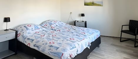 Un dormitorio con una cama, mesitas de noche, una silla y una lámpara de pared.