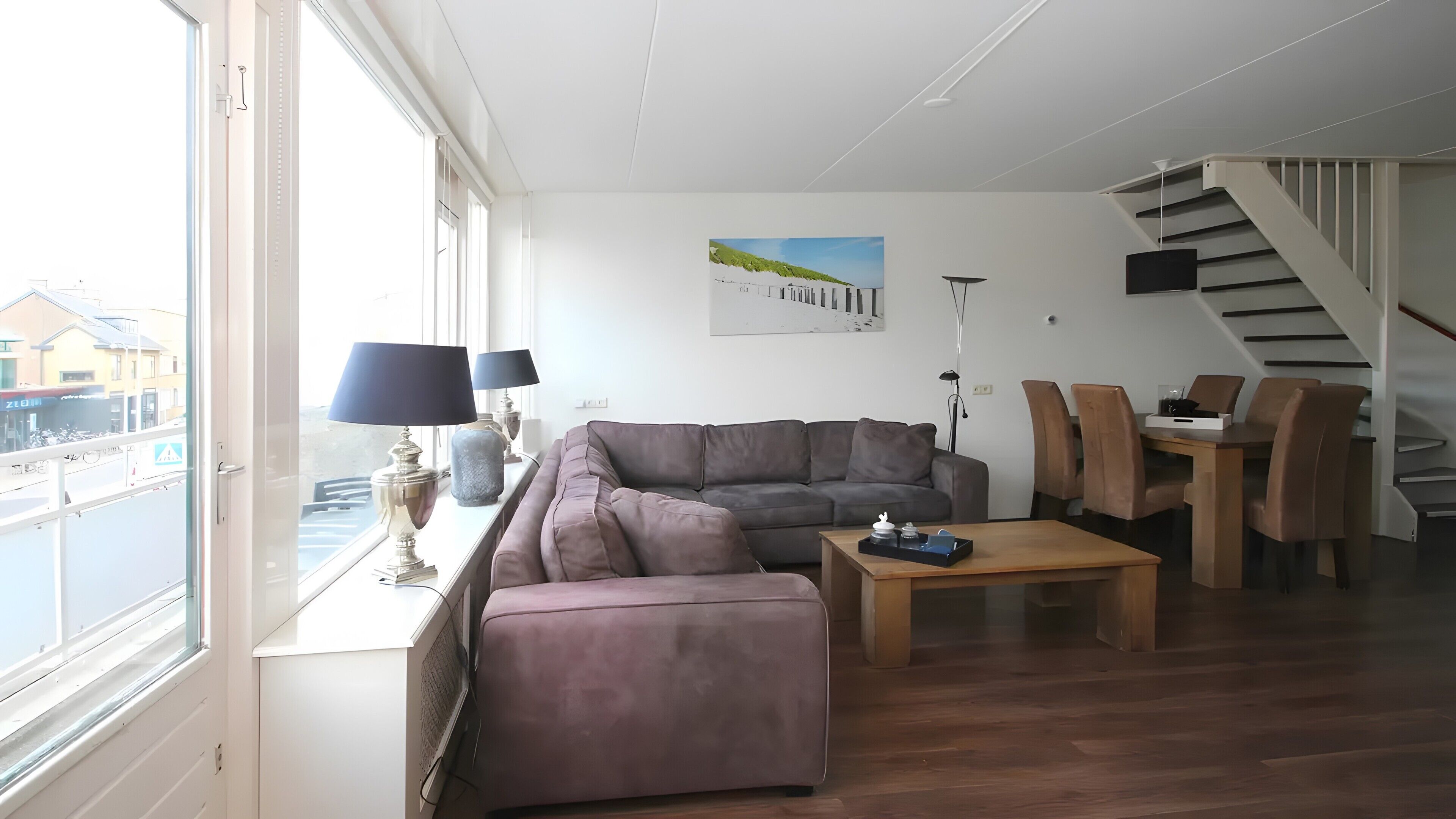 Ein Wohnzimmer mit einer Couch, einem Couchtisch und einem Essbereich mit Stühlen. Ein Fenster bietet Blick auf Gebäude außerhalb.