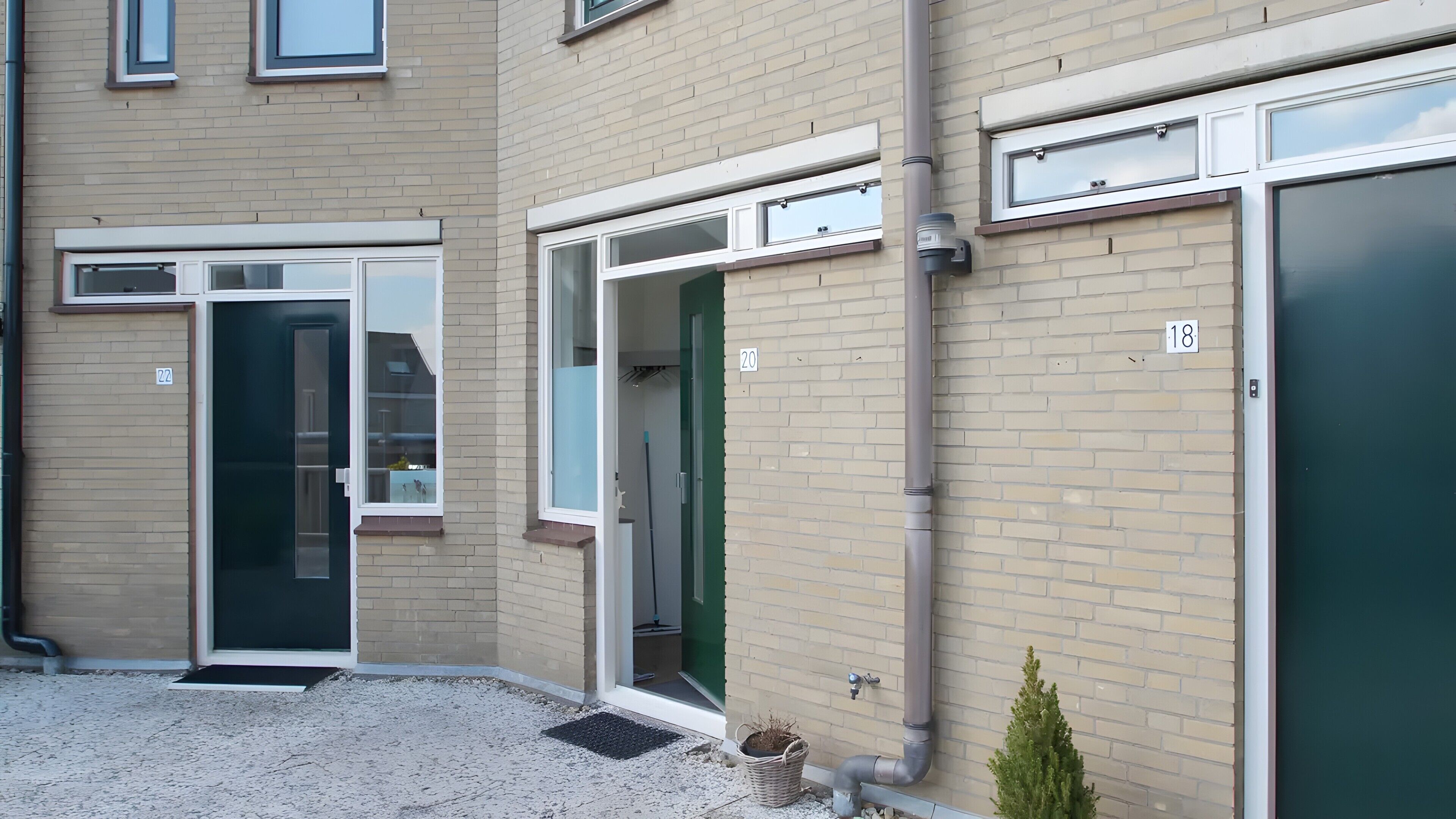 Ein Gebäude mit nummerierten Türen, einer kleinen Pflanze und einer Leitungsverrohrung.