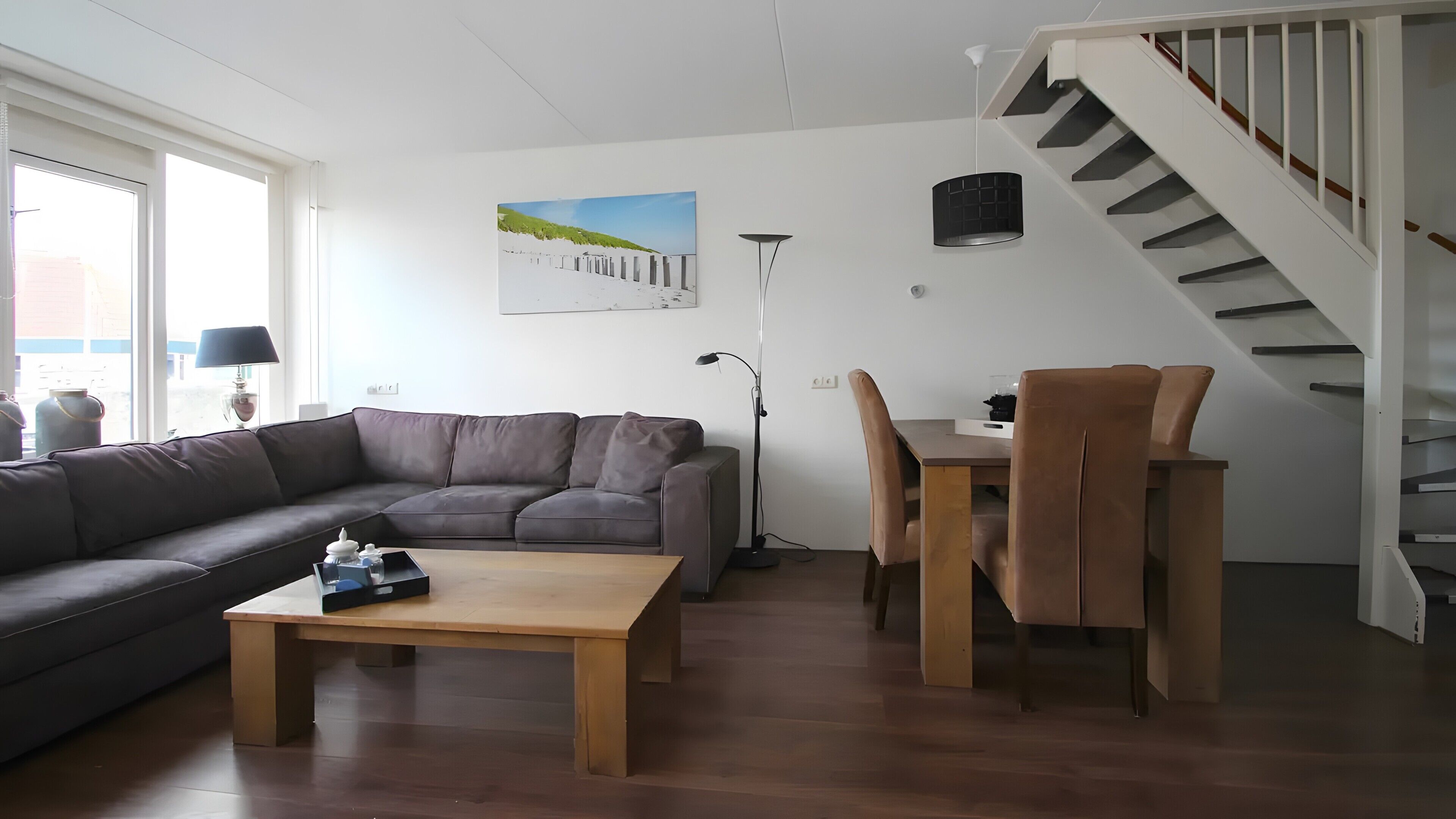 Un salon comprenant un canapé, une table basse, une table à manger avec des chaises, un lampadaire et un escalier.