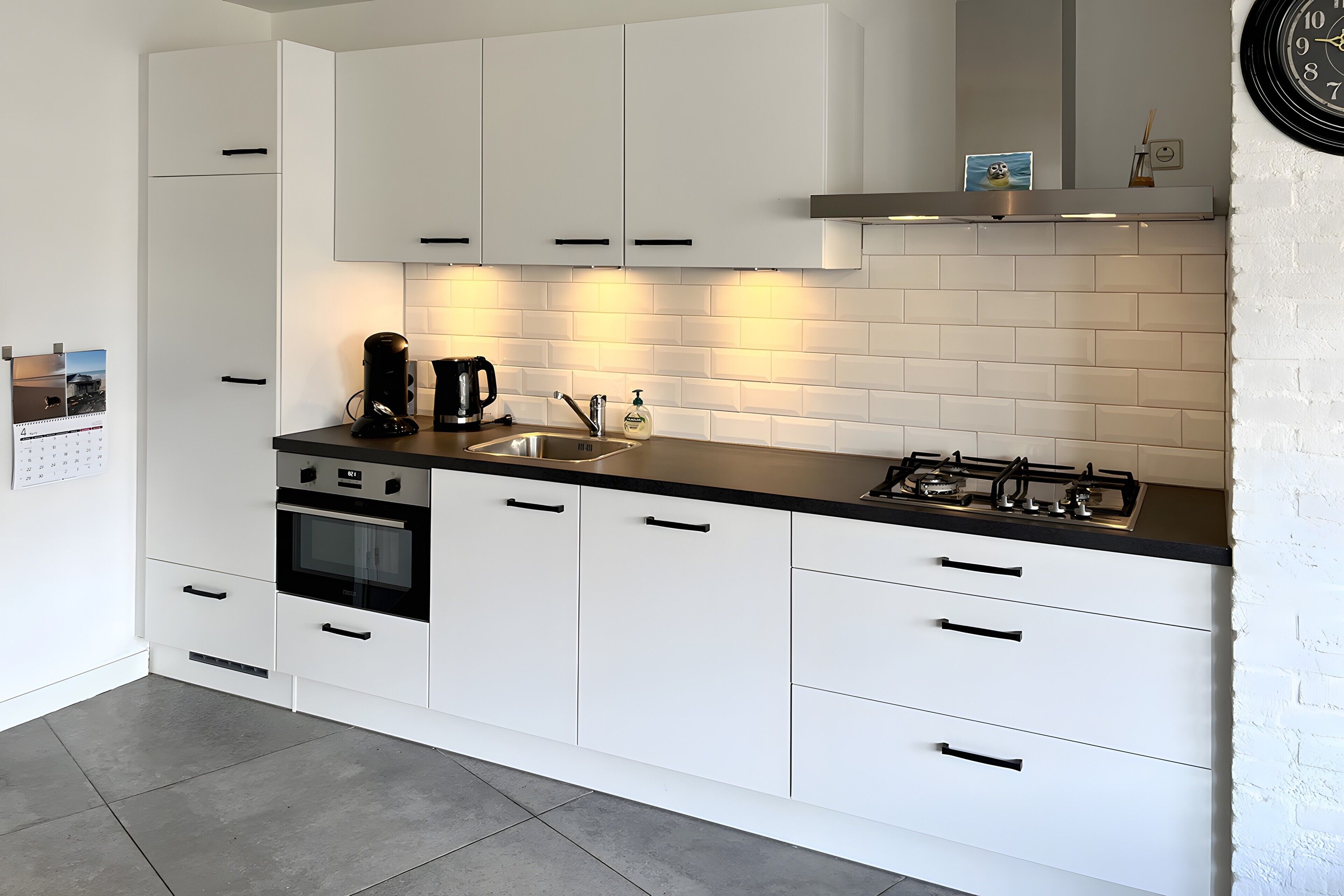 A modern kitchen with white cabinets, a black countertop, a gas stove, and a coffee maker.