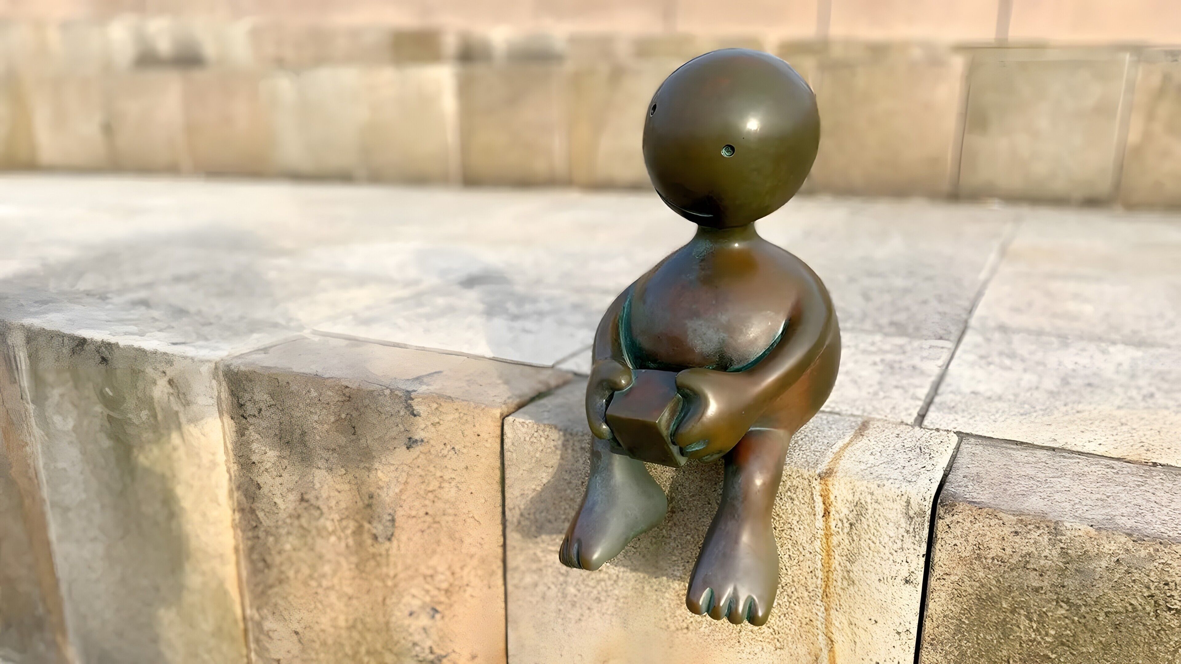 Una estatua de bronce muestra una figura sentada sobre un pedestal de piedra.