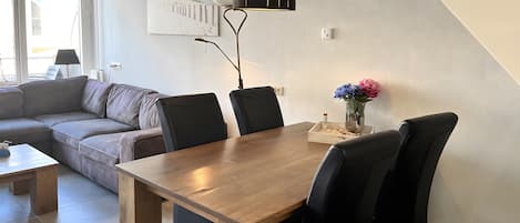 Een moderne woonkamer met een houten eettafel, zwarte stoelen, een bank en een schilderij aan de muur.