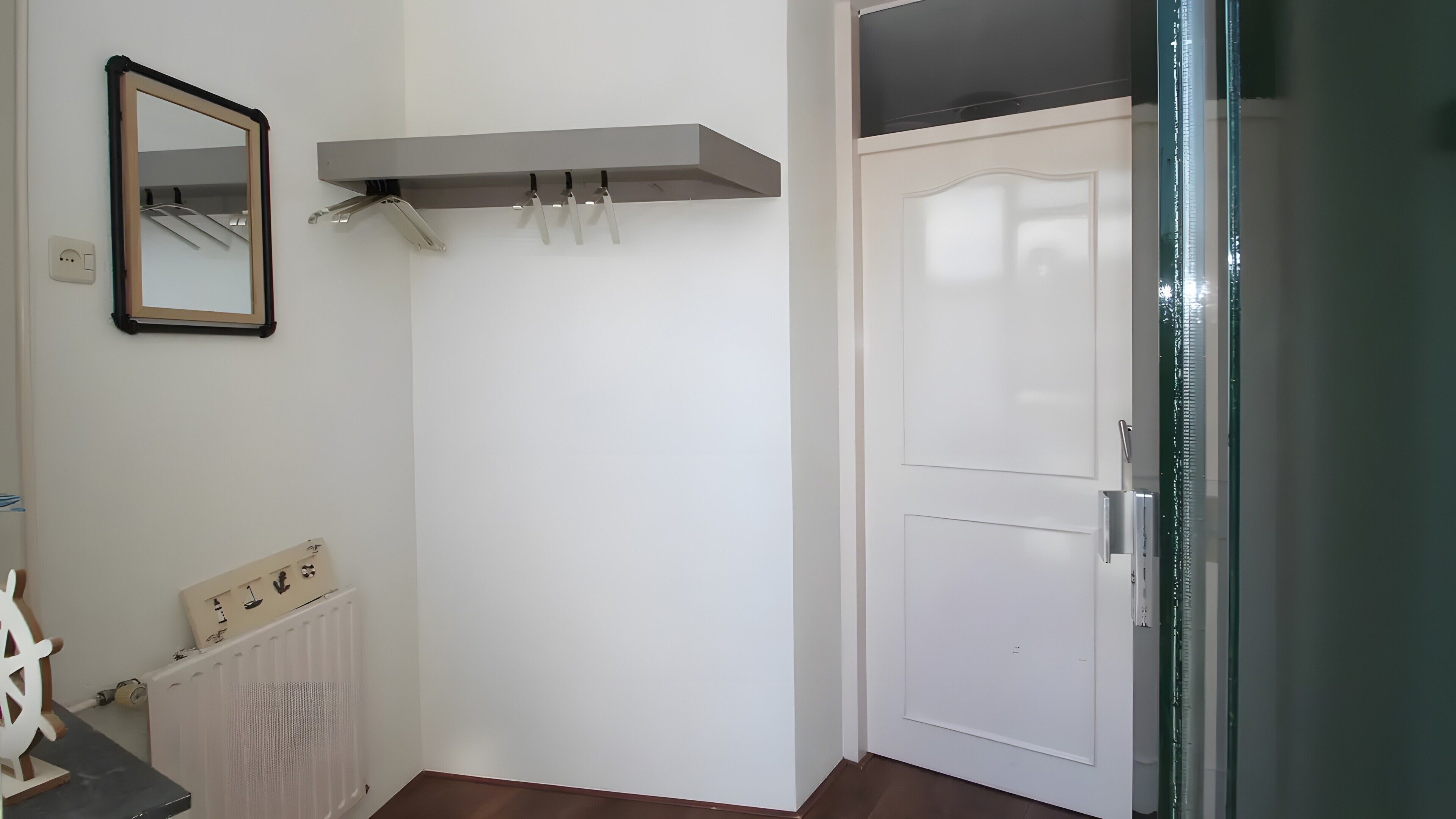 Een kamer met een witte deur, een radiator, een spiegel en een kapstok.