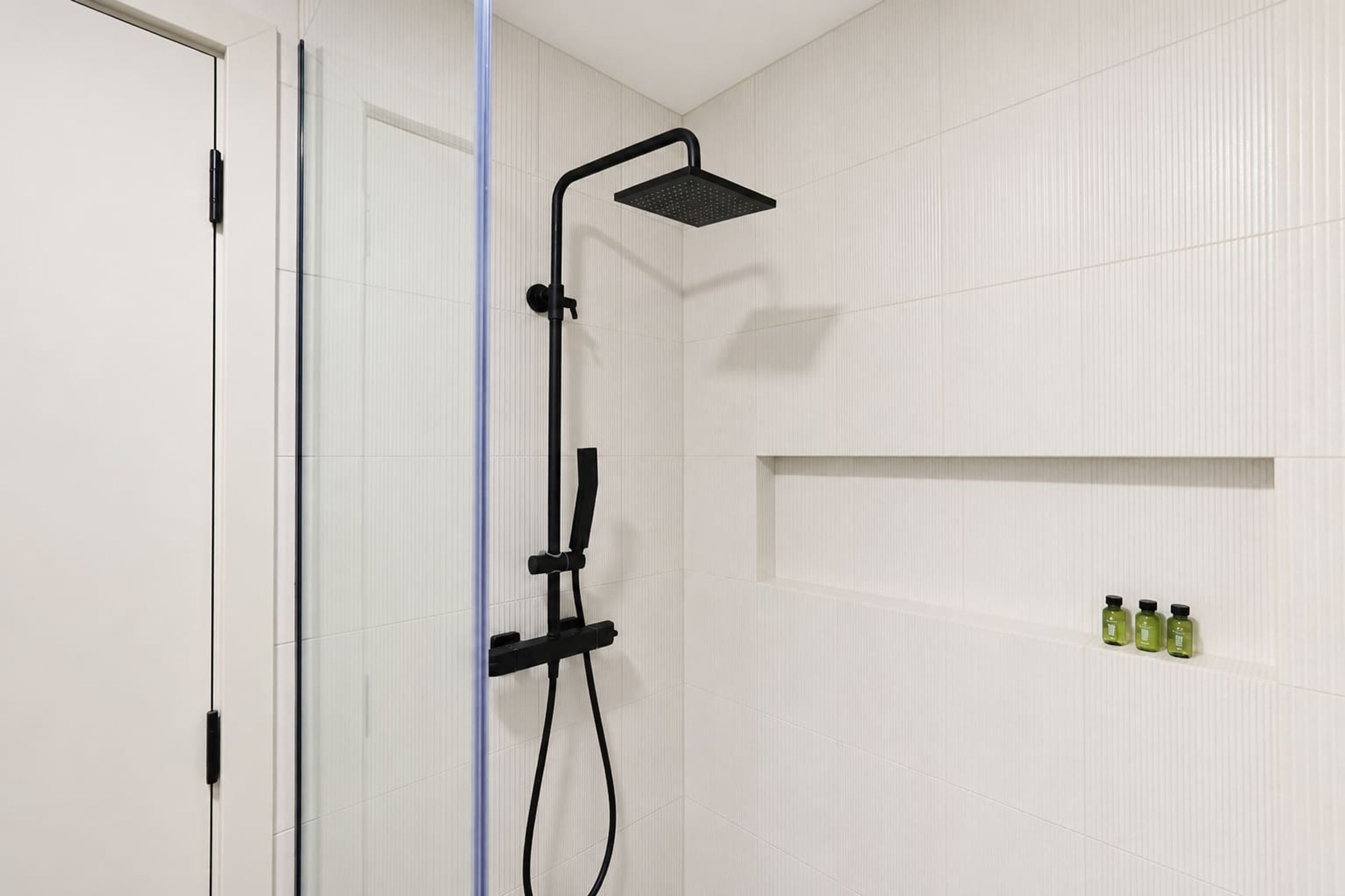 A modern bathroom with a shower, a glass door, and a shelf with toiletries.
