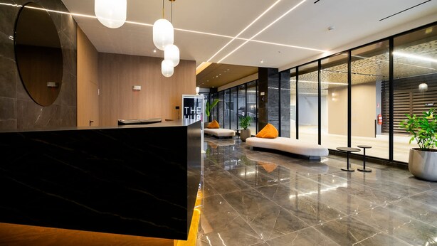 A modern reception area with a marble reception desk, a seating area with orange cushions, and a glass wall. - w Enchanting 2BR w Balcony in San Francisco (Panama City)