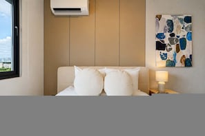 Ein Hotelzimmer mit einem Bett, einem Nachttisch, einer Lampe, einer Klimaanlage und einem Bild an der Wand.