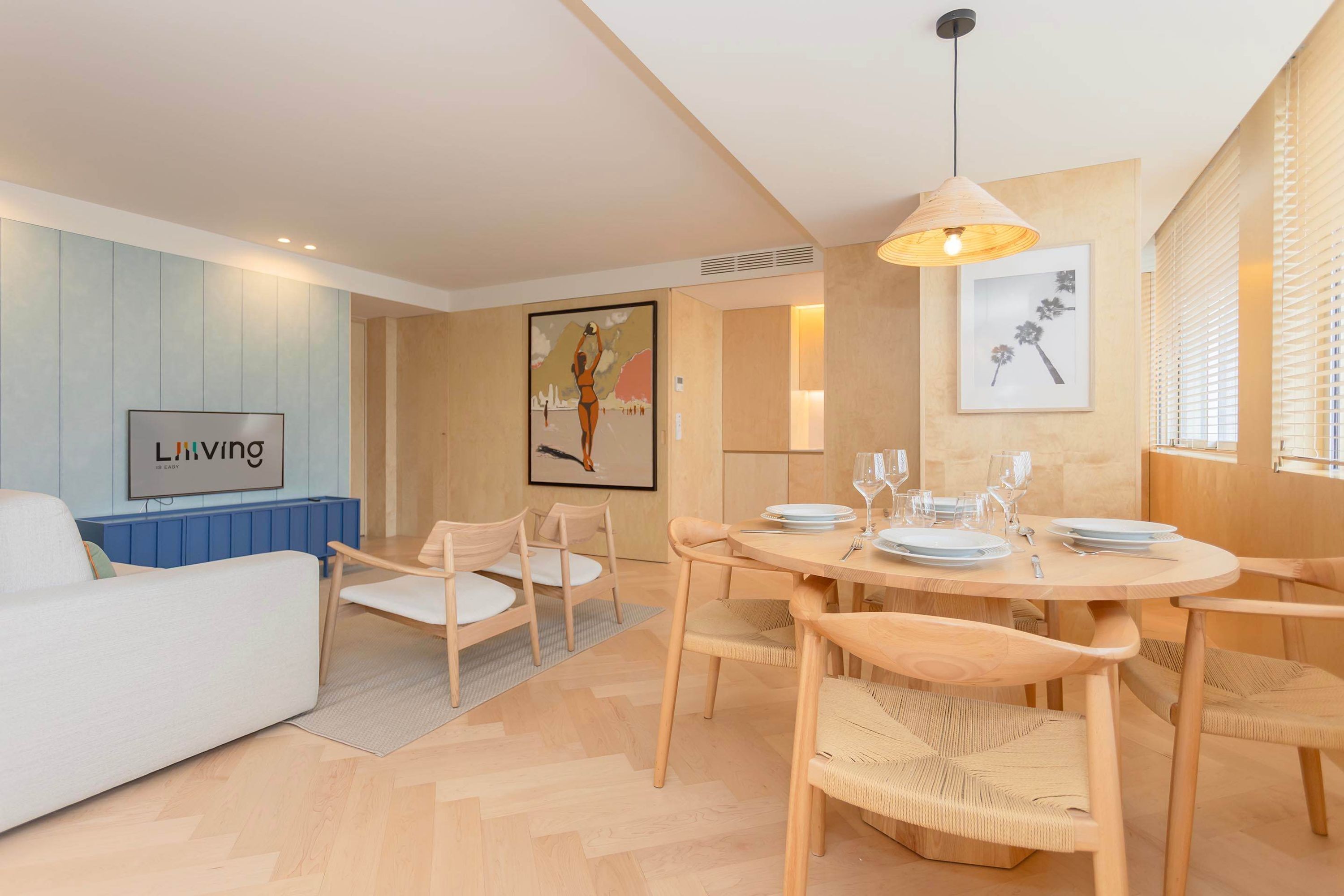 A modern living room with a white sofa, a dining table set for four, and a large painting on the wall.