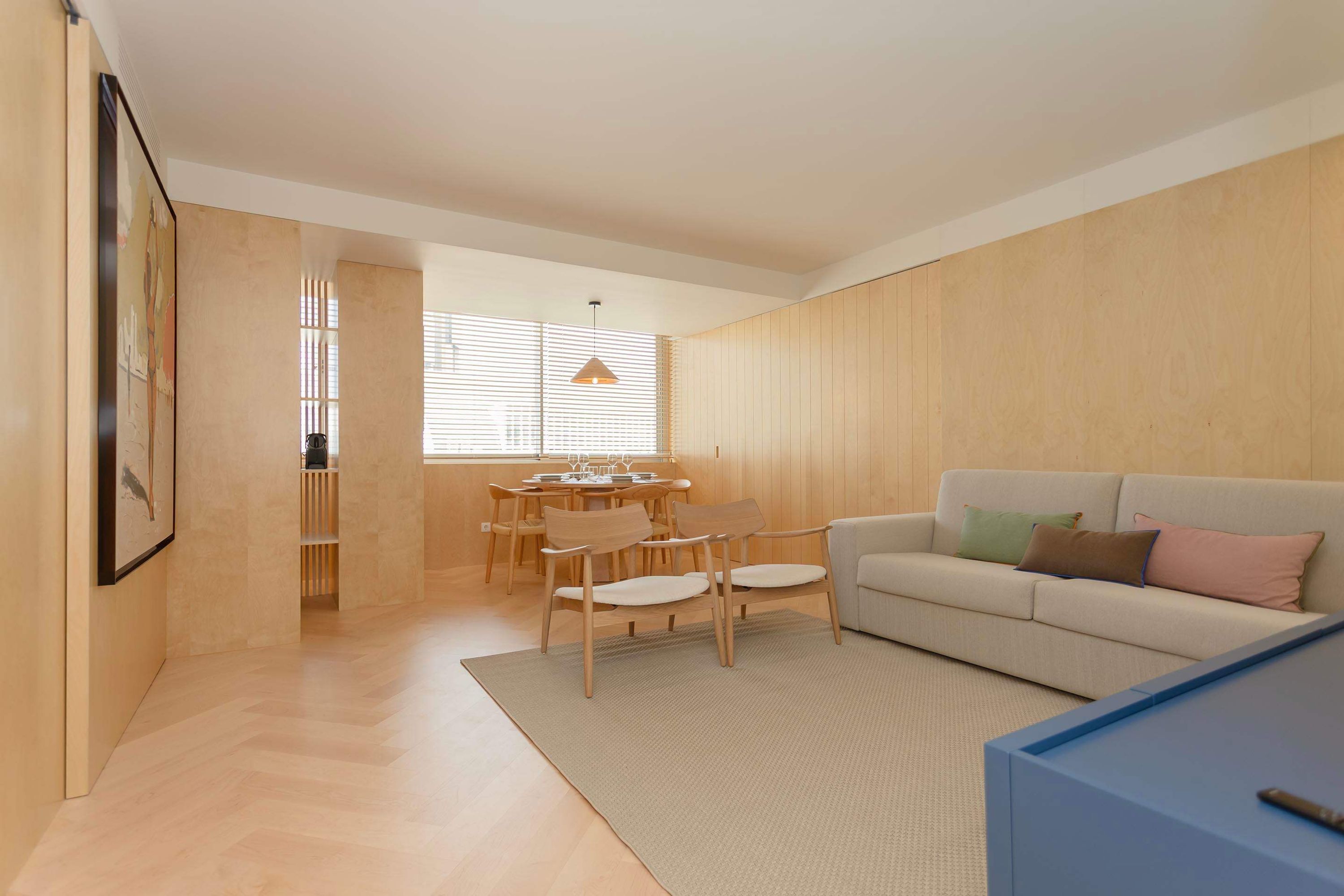 A modern living room with a sofa, chairs, a dining table, and a kitchen area.