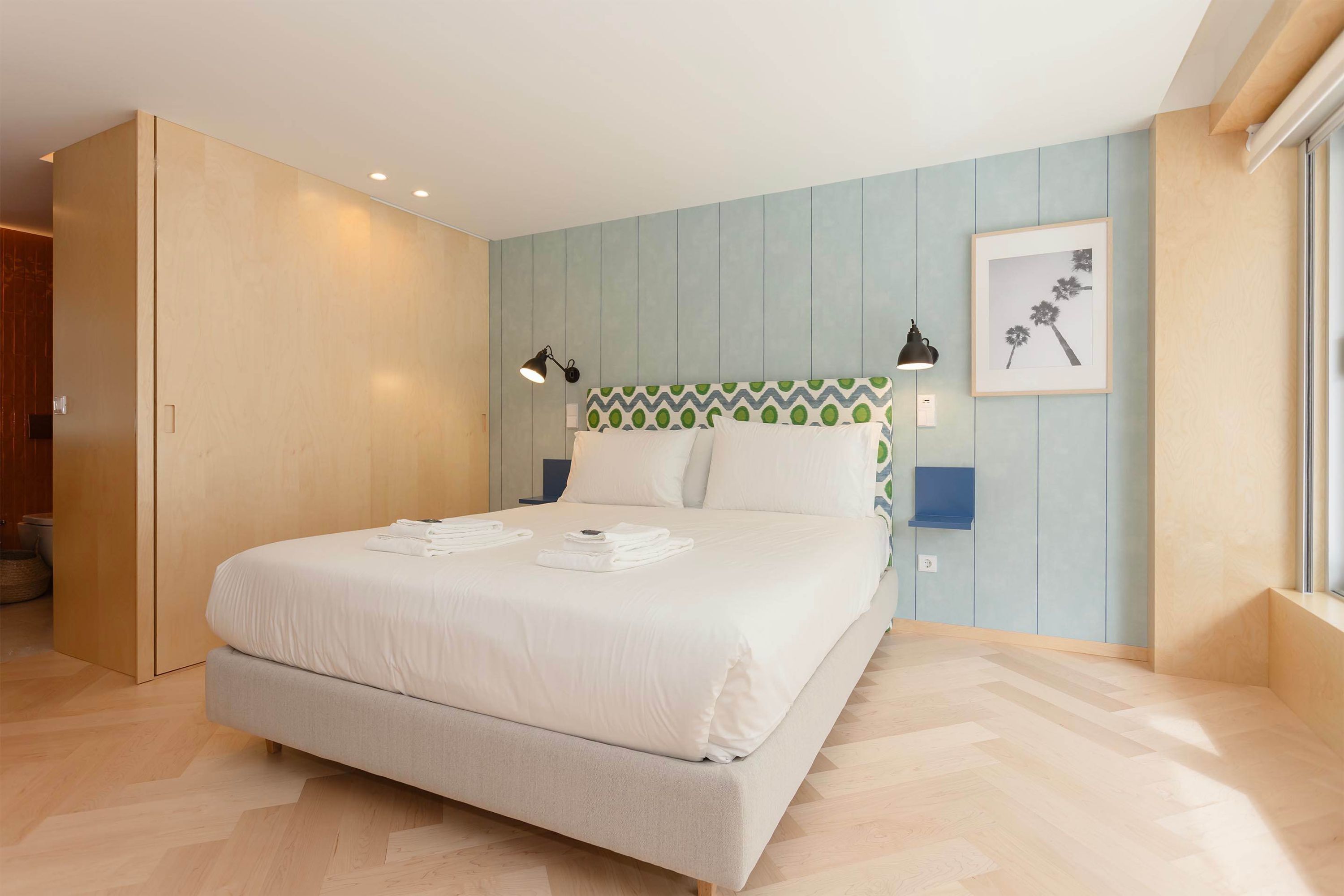 Une chambre d’hôtel avec un lit, des lampes de chevet, un tableau encadré au mur et une fenêtre.