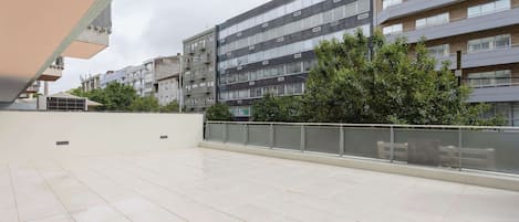 Una amplia terraza exterior con suelo de baldosas, rodeada de edificios modernos con numerosas ventanas y balcones.
