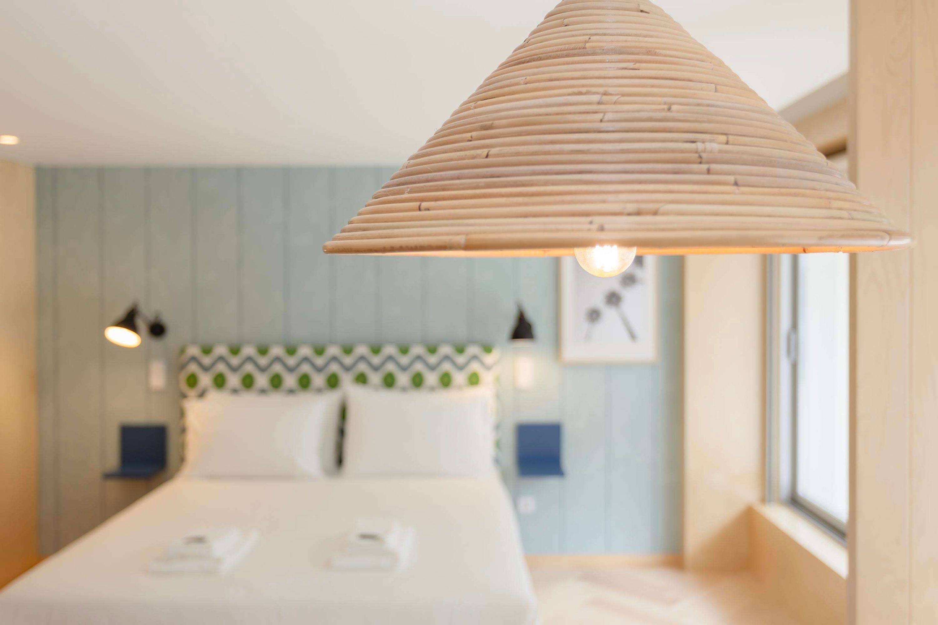 A hotel room with a bed, a hanging light fixture, and a window.
