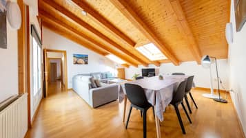 Een ruime loft met een hoge houten plafond, een eethoek met tafel en stoelen, een bank en een televisie.