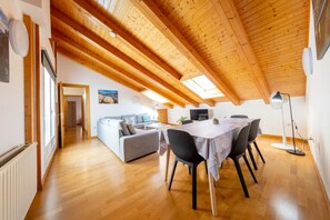 Ein geräumiges Loft mit einer hohen Holzbalkendecke, einem Essbereich mit Tisch und Stühlen, einer Couch und einem Fernseher.