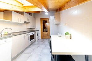 Cocina compacta con techo de madera, horno integrado, lavadora y un pequeño comedor con mesa y sillas.