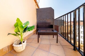 A balcony with a wicker chair, a potted plant, and a metal railing.