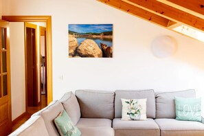 Ein Wohnzimmer mit grauem Sofa, einem Landschaftsbild und einer Holzzieldecke.