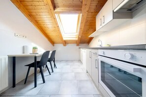 A modern kitchen with a skylight, white cabinets, a dining table with chairs, and a built-in oven.