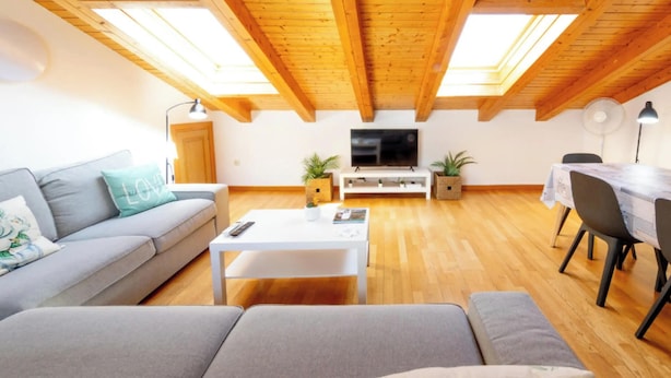 A modern living room with a sofa, a coffee table, a TV, and a dining area with chairs and a table.