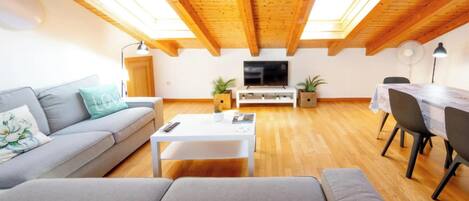 A modern living room with a sofa, a coffee table, a TV, and a dining area with chairs and a table.