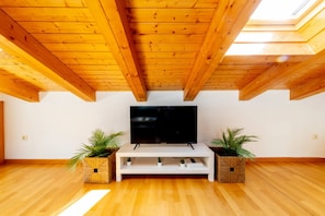 A room with a wooden ceiling, a flat-screen TV on a white stand, and two potted plants on either side.