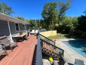 Una terraza de madera con mobiliario exterior, piscina y jardín vallado.