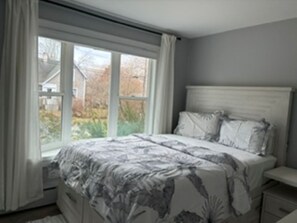 Un dormitorio con una cama, una mesita de noche y un ventanal con cortinas.