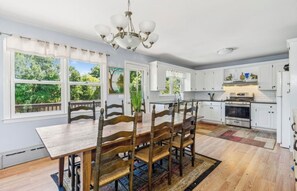 A kitchen with white cabinets, a wooden dining table, and chairs. There is a chandelier above the table.