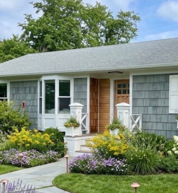 A single-story house with a front porch, a small entryway, and a garden with various plants and flowers.