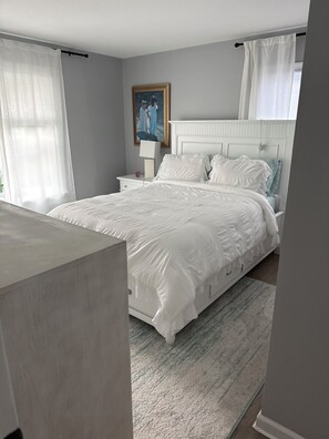 A bedroom with a large bed, a nightstand, a lamp, and a painting on the wall.