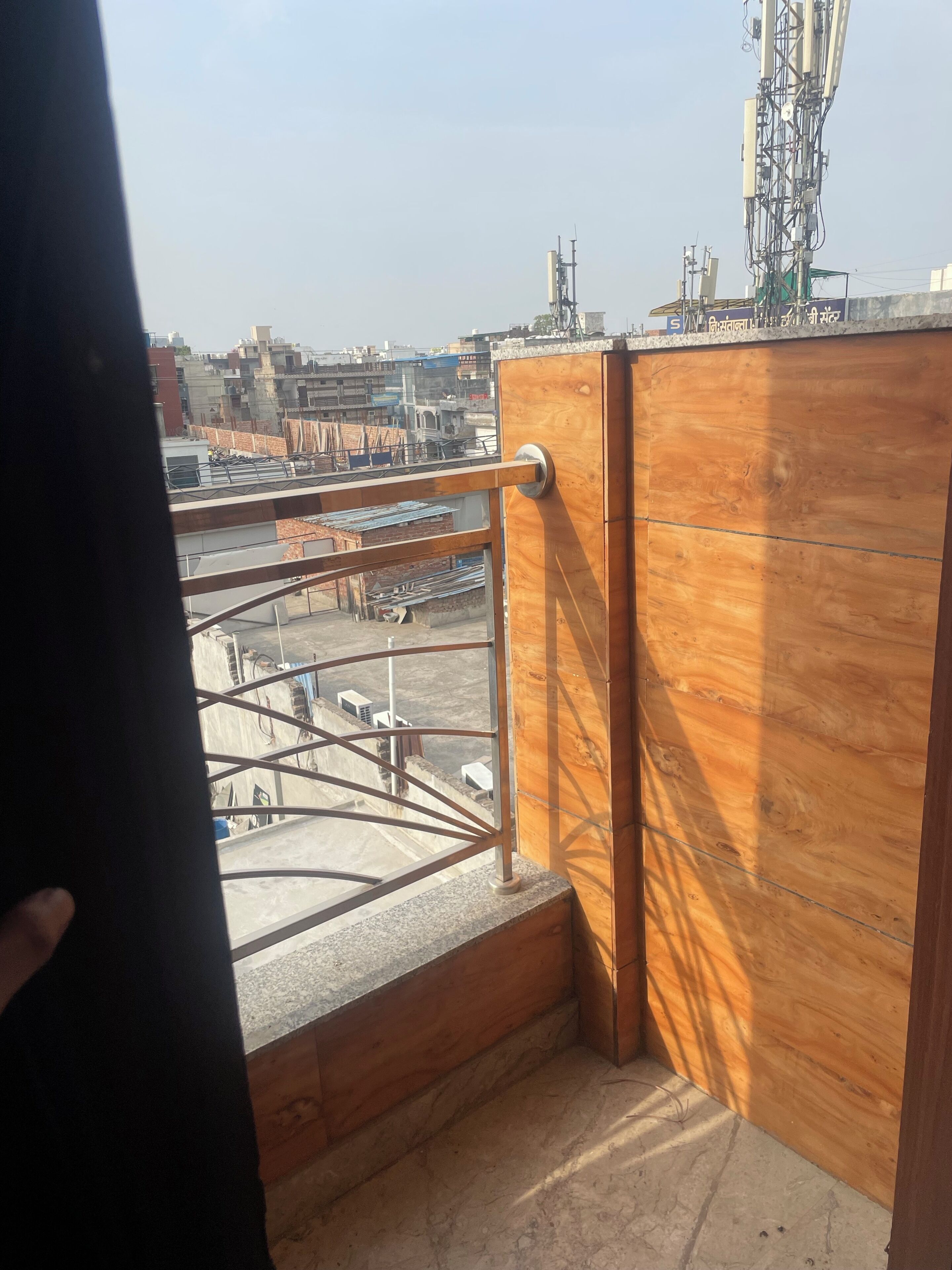 Un balcon doté d’une rambarde en métal, d’un lambris en bois et offrant une vue sur un paysage urbain avec des bâtiments et du matériel de construction.