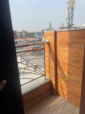 A balcony with a metal railing, wooden paneling, and a view of a cityscape with buildings and construction equipment.