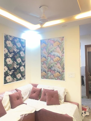 A room with a bed, two wall-mounted paintings, and a ceiling fan.