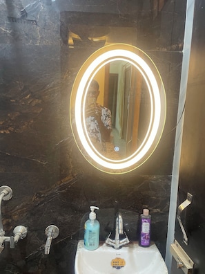 A bathroom with a marble sink, a mirror with a light, and a shower.