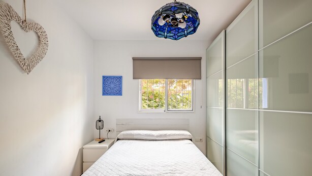 A bedroom with a bed, a nightstand, a lamp, a decorative heart, a blue wall art, a window with a view, and a ceiling light fixture. - Holiday Home 'Villa La Mayorazga Cozy Cottage' with Private Pool, Private Terrace and Wi-Fi (Pago del Humo)