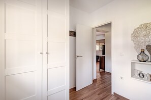 Ein Flur mit weißen Türen, Holzboden und einer Küche im Hintergrund.