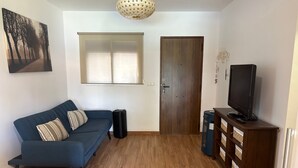 A living room with a blue sofa, a television on a wooden stand, a door, and a window with blinds. - Holiday Home 'Villa La Mayorazga Cozy Cottage' with Private Pool, Private Terrace and Wi-Fi (Pago del Humo)