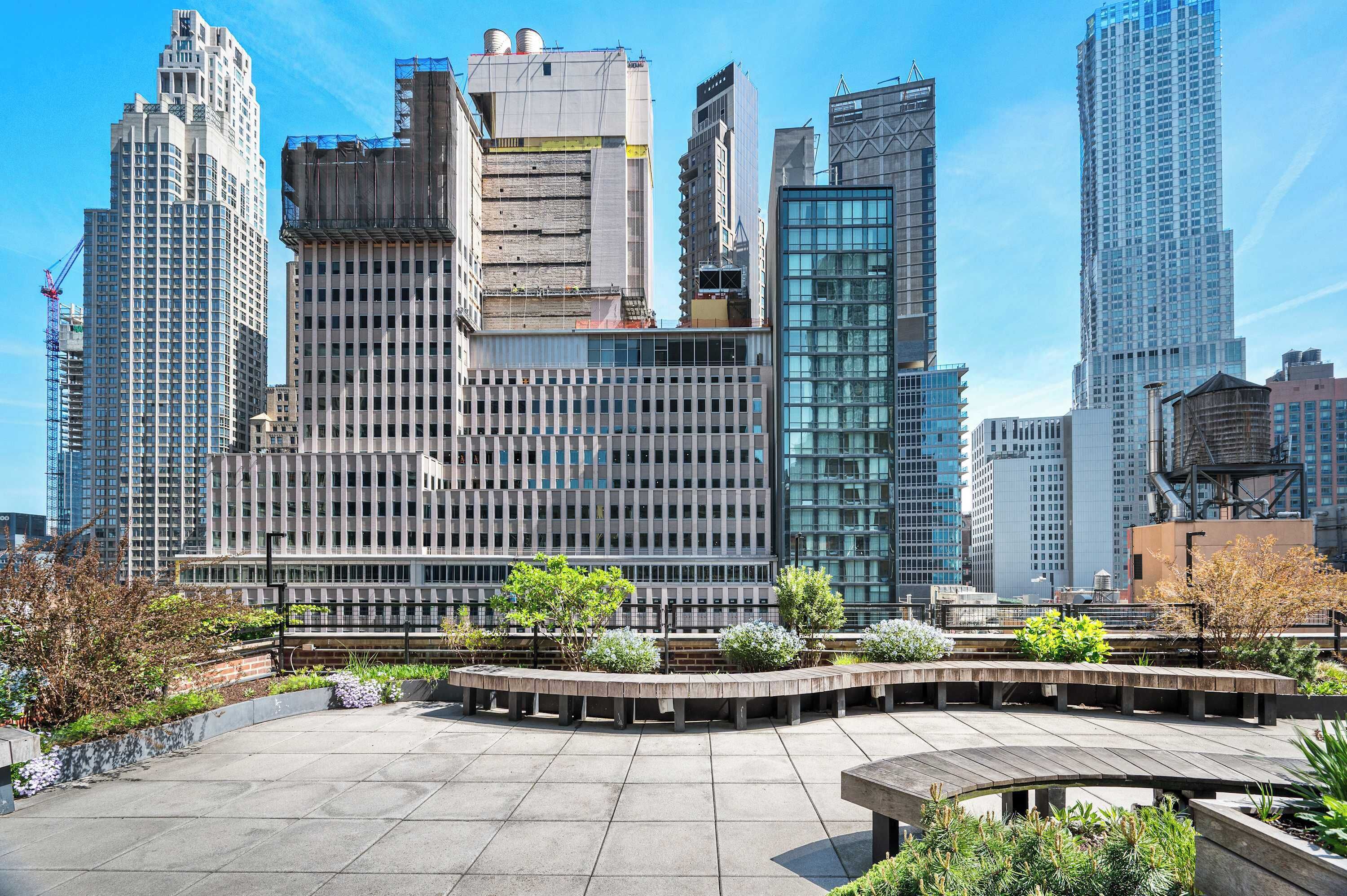 A modern urban plaza with a variety of buildings, including a large glass-fronted structure and a building with a grid-like facade.