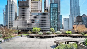 Una plaza urbana moderna con diversos edificios, incluyendo una gran estructura con fachada de vidrio y un edificio de fachada enrejada.
