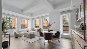 Un salon moderne avec un canapé, une table basse et une table à manger. De grandes fenêtres offrent une vue sur la ville.